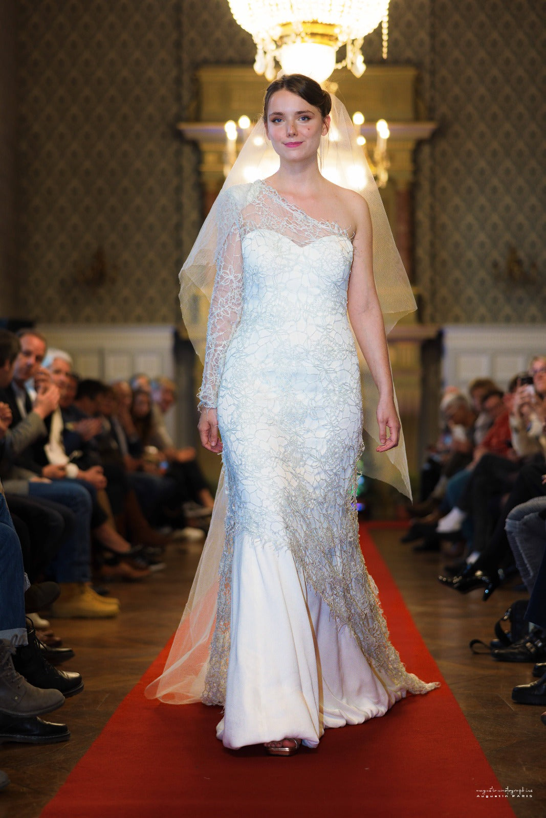 Robe de mariée Forever & Ever Ousman O. en dentelle de soie et crêpe de soie, avec manches longues transparentes, coupe asymétrique et grand voile en soie, présentée lors d’un défilé.