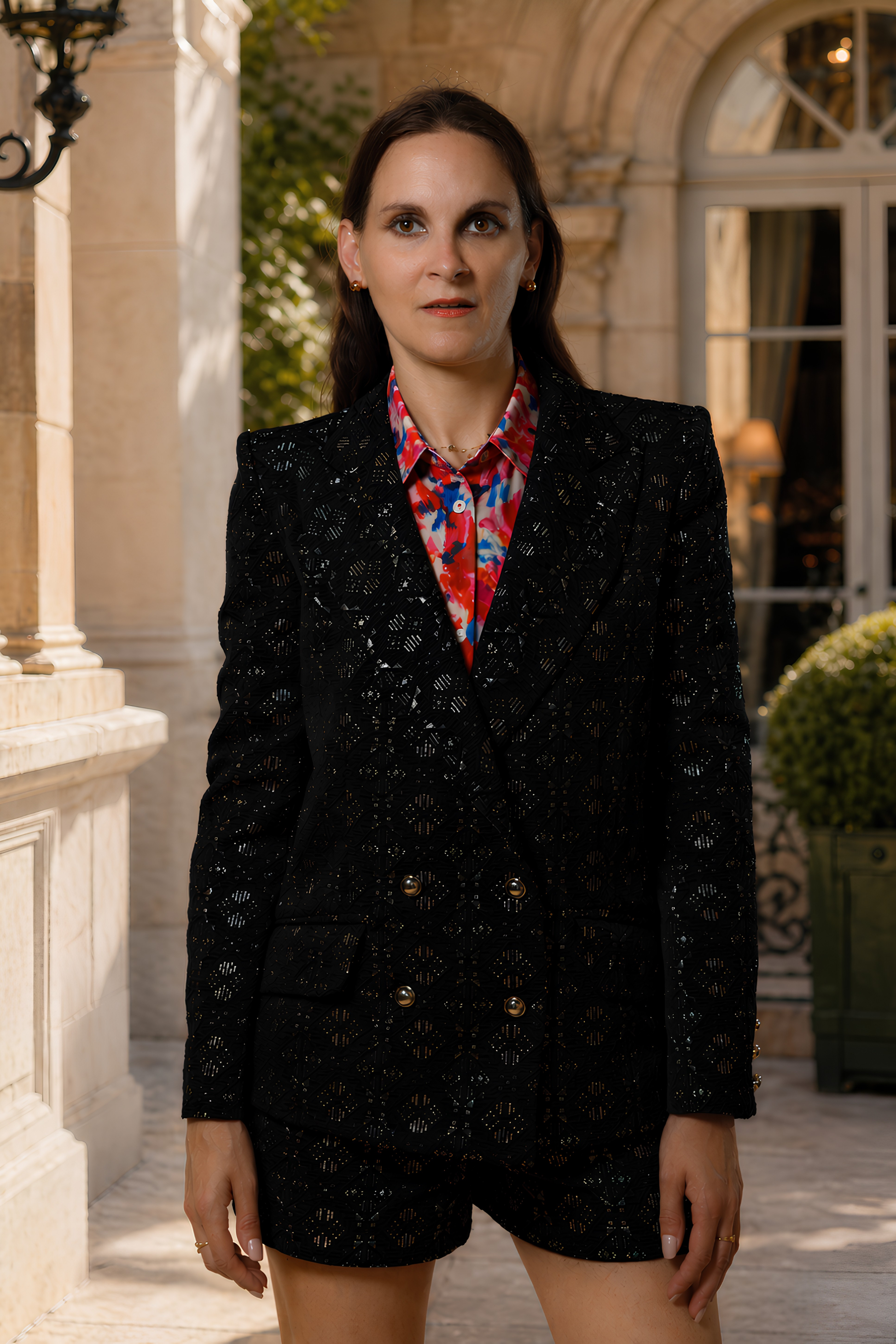 Femme portant l’Ensemble Brocart Tailleur croisé noir Ousman O. devant une architecture en pierre.
