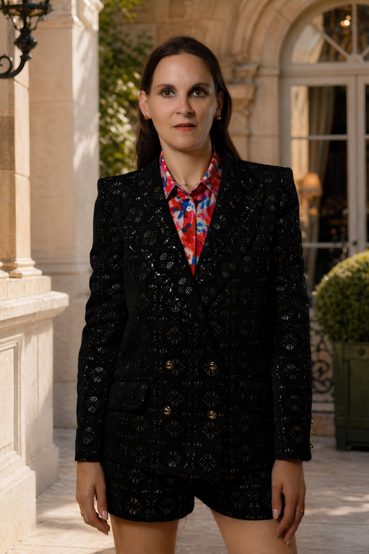 Femme portant l’Ensemble Brocart Tailleur croisé noir Ousman O. devant une architecture en pierre.