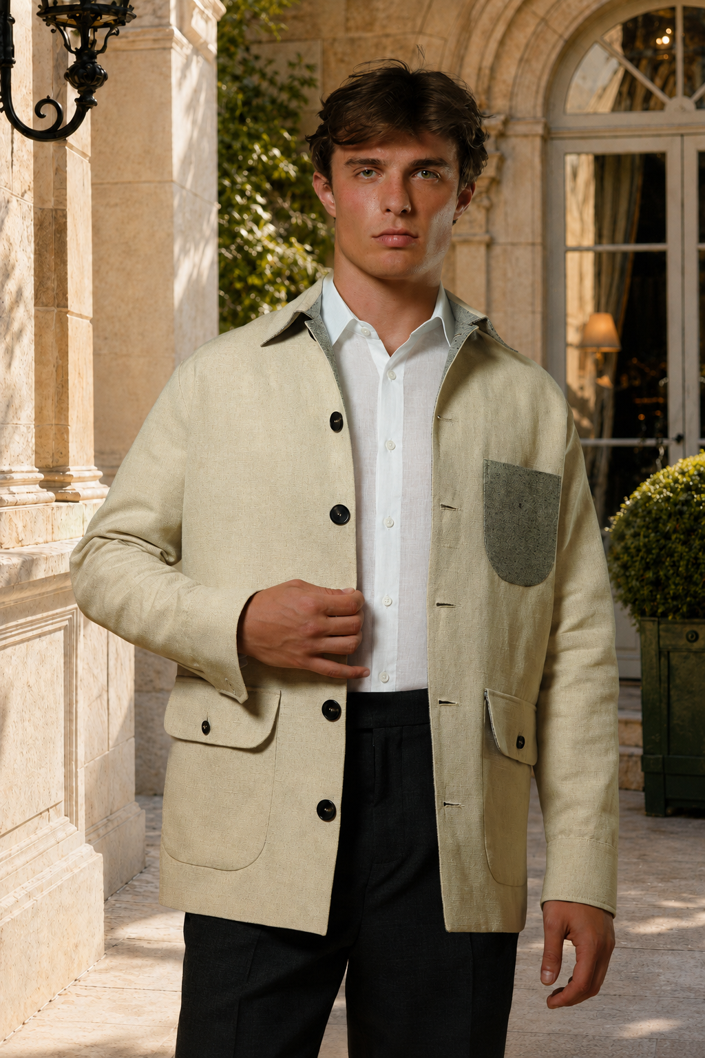 Mannequin portant la Veste Atelier Riviera en chanvre écru, avec poche poitrine grise contrastée, devant une architecture en pierre.